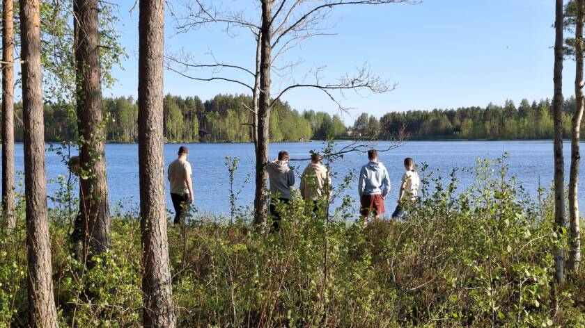 Joukko nuoria metsäisellä järvenrannalla.