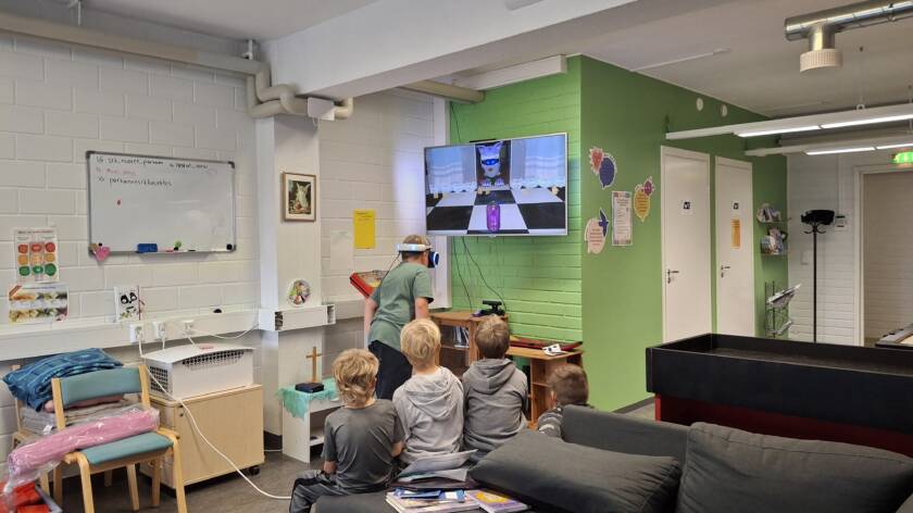 Joukko lapsia nuortentilassa, yksi pelaa virtuaalitodellisuus-peliä ja muut katsovat vierestä.