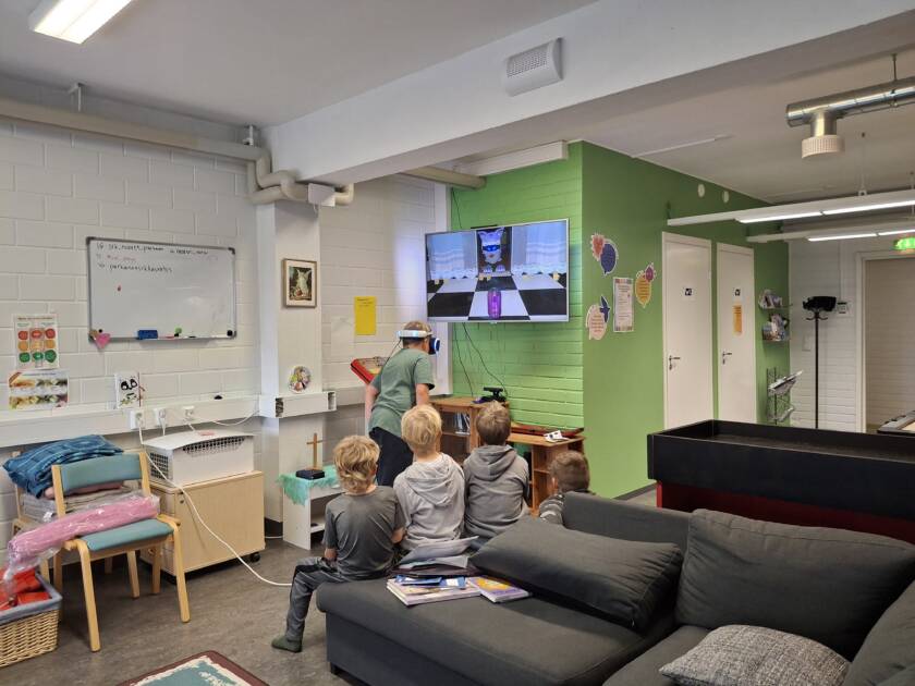 Joukko lapsia nuortentilassa, yksi pelaa virtuaalitodellisuus-peliä ja muut katsovat vierestä.