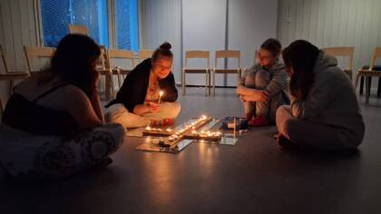 Ohjaaja Mirja ja kolme nuorta kynttilänvalossa, tuikkukynttilät on aseteltu lattialle ristinmuotoon.
