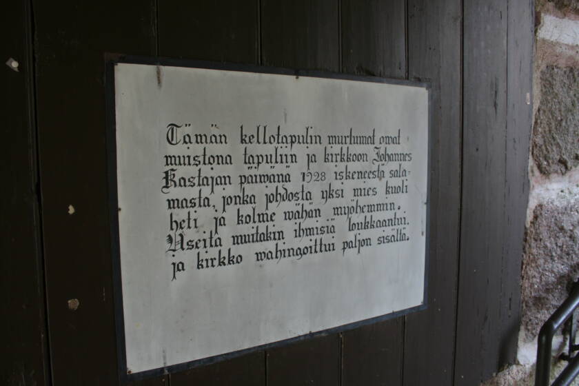 Plakaatti kellotapulin sisällä, jossa lukee "Tämän kellotapulin murtumat ovat muistona tapuliin ja kirkkoon Johannes Kastajan päivänä 1928 iskeneestä salamasta, jonka johdosta yksi mies kuoli heti ja kolme vähän myöhemmin. Useita muitakin ihmisiä loukkaantui, ja kirkko vahingoittui paljon sisältä."