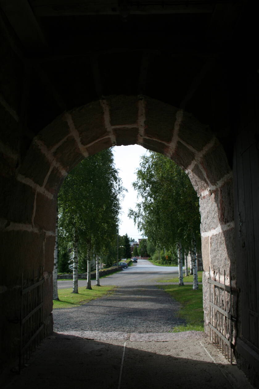 Kellotapulin holvikaari kuvattuna sisältä, ulkona näkyy koivuja ja katua.