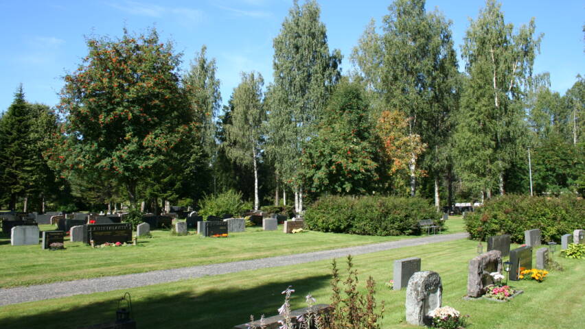 Hautakiviä nurmella, taustalla eri lehtipuita.
