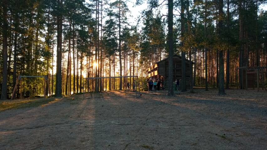 Puiden takaa siivilöityvä auringonlasku leirikeskuksella.