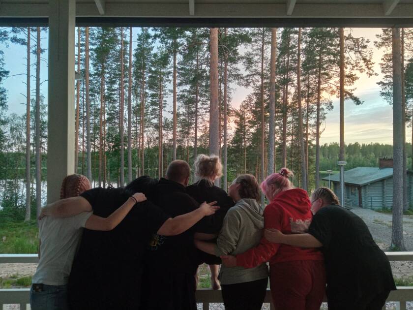 Joukko nuoria halaamassa toisiaan leirikeskuksella auringonlaskun aikaan.