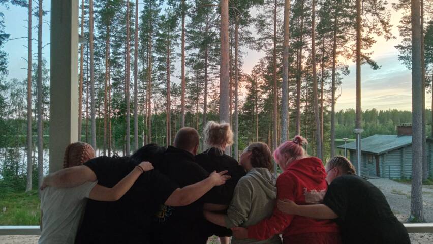 Joukko nuoria halaamassa toisiaan leirikeskuksella auringonlaskun aikaan.